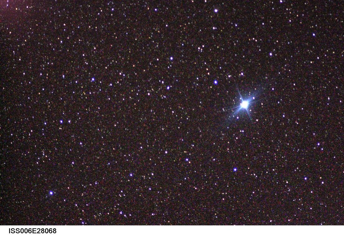 Fotografia noturna feita do espaço: estrela muito brilhante, Canopus, sobre o horizonte escuro e curvo da Terra.