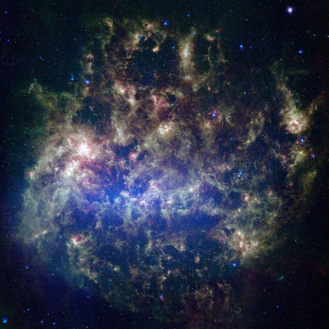 Galáxia irregular vista em infravermelho, com uma barra central azulada de estrelas e nuvens avermelhadas e esverdeadas de poeira espalhadas ao redor.