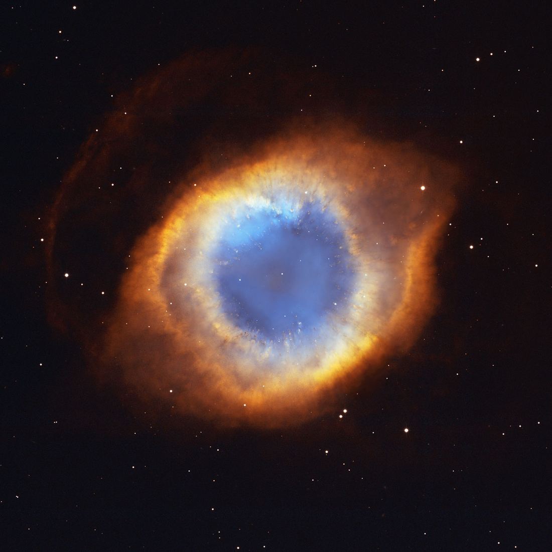 Grande anel de gás em tons de azul e vermelho visto de frente, lembrando um olho, com uma estrela branca pequena no centro e milhares de pequenos glóbulos na borda interna.